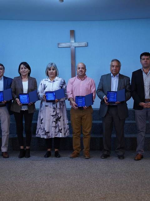 Un grupo de personas posando en un escenario con trofeos en un ambiente formal.