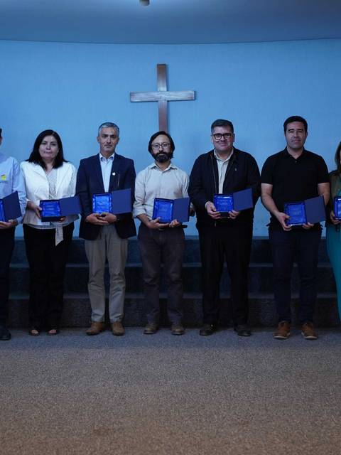 Un grupo de personas sonrientes sostiene certificados frente a un fondo azul con una cruz.