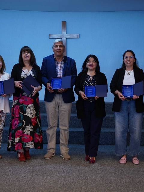 Un grupo de personas posando en un escenario con un fondo de luz azul y una cruz en la pared.