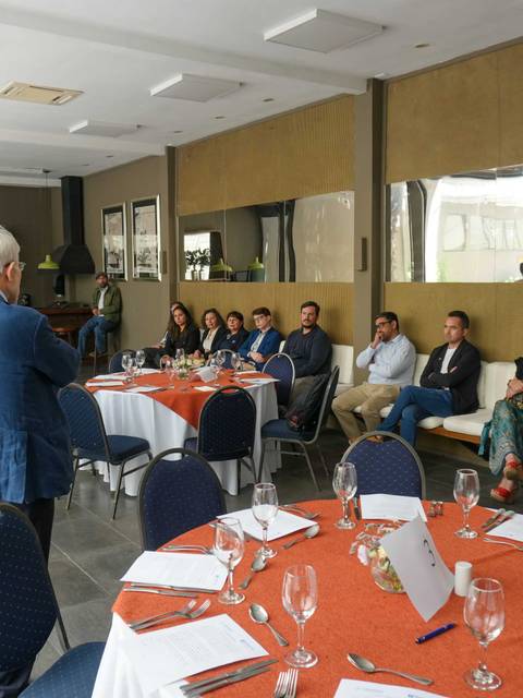 Un grupo de personas asistentes a una reunión en un salón con mesas decoradas.