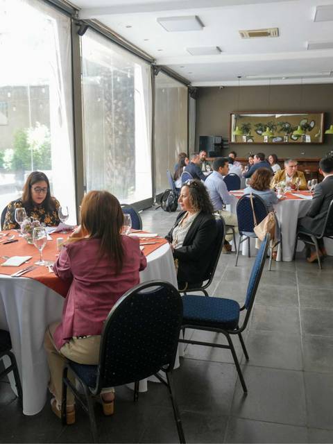 Un grupo de personas se reúne en un salón con mesas redondas en un ambiente luminoso.