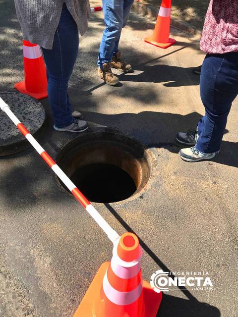 Una zona de trabajo con un agujero visible en el suelo, rodeado de conos de seguridad y cinta de advertencia.