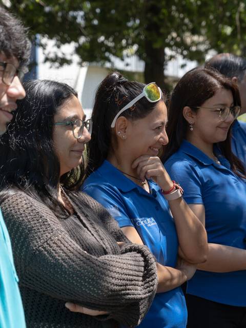 Un grupo de personas sonriendo y conversando al aire libre, vestidas con camisetas azules.