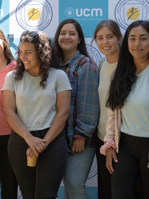 Un grupo de mujeres posando juntas mientras sostienen a un bebé frente a un fondo con el logo de UCM.