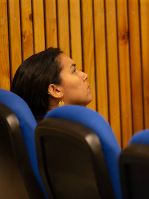 Una mujer sentada en una silla, mirando hacia arriba en un ambiente interior.