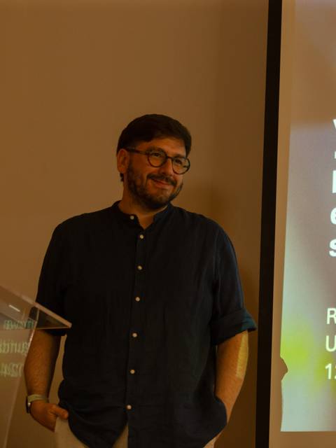 Un hombre sonriente presenta un tema sobre ética y sostenibilidad en la investigación de seres vivos.