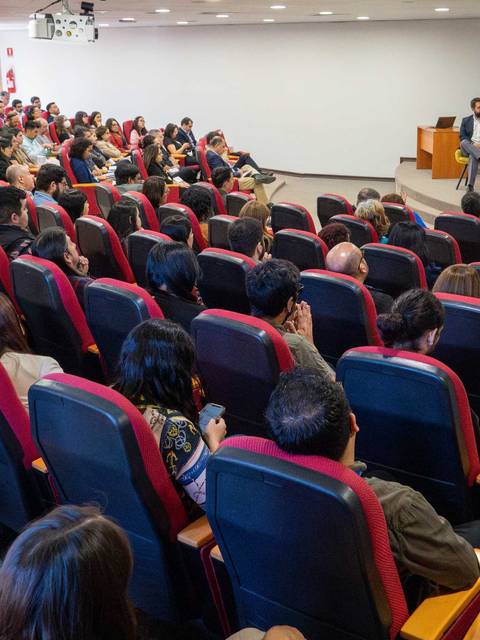 Una conferencia con un gran público en un salón, donde se realiza un panel de discusión.