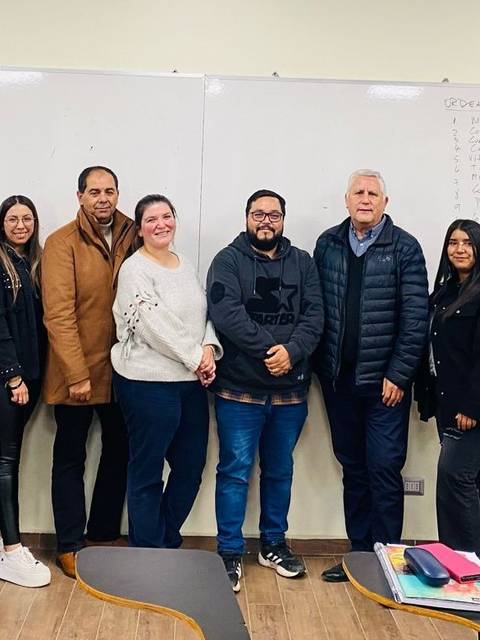 Un grupo de personas posando juntas en un aula con un pizarrón blanco al fondo.