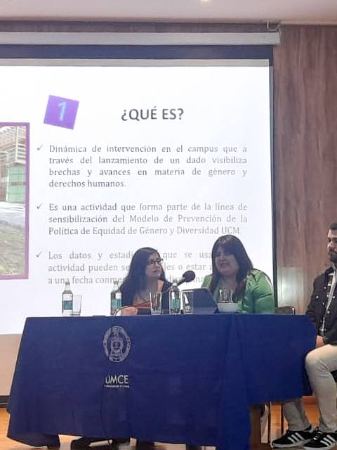 Una mesa de debate en un auditorio con tres personas hablando frente a una presentación visual sobre derechos humanos.
