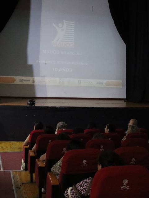 Una conferencia está teniendo lugar en un auditorio con un orador en el podio y la audiencia sentada frente a él.
