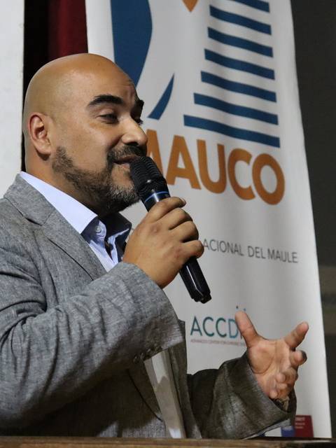 Un hombre gesticula mientras habla con un micrófono en mano durante un evento.