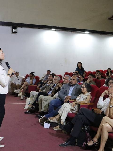 Una ponente está dando una charla frente a un público sentado en un auditorio.
