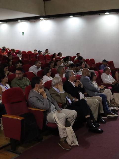 Una conferencia en un auditorio con un gran número de asistentes sentados.