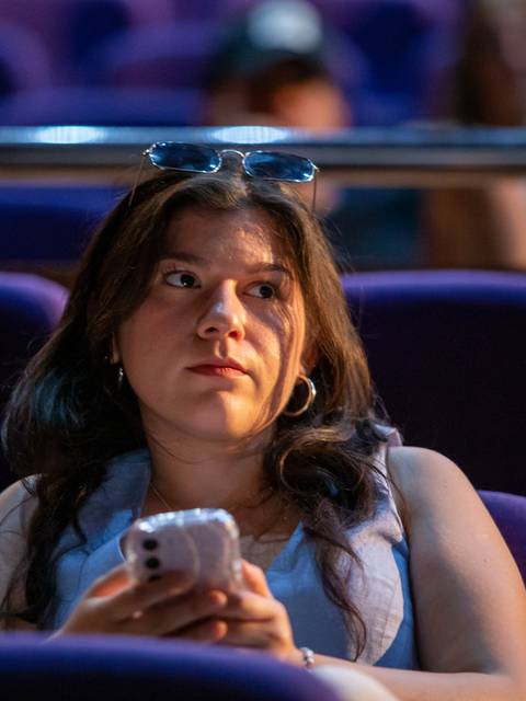 Una joven sentada en una sala con asientos morados, mirando su teléfono móvil con atención.