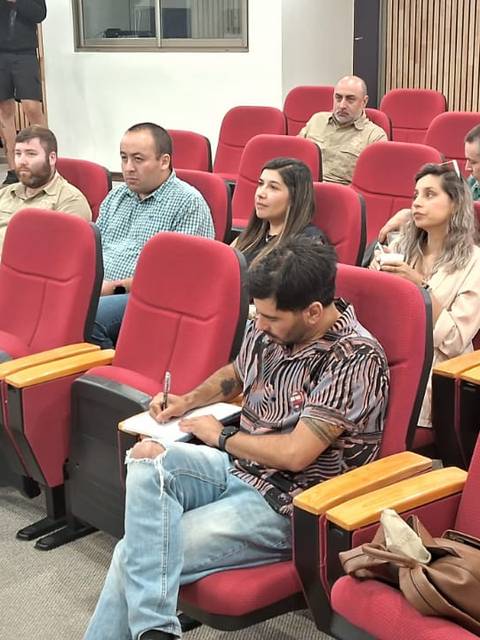 Una reunión en un auditorio con un presentador y un grupo de asistentes sentados en filas.