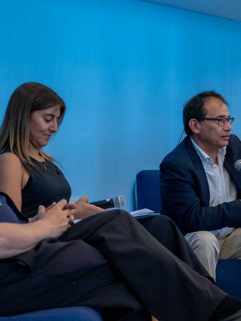 Un panel de discusión con tres personas sentadas en un escenario con fondo azul.