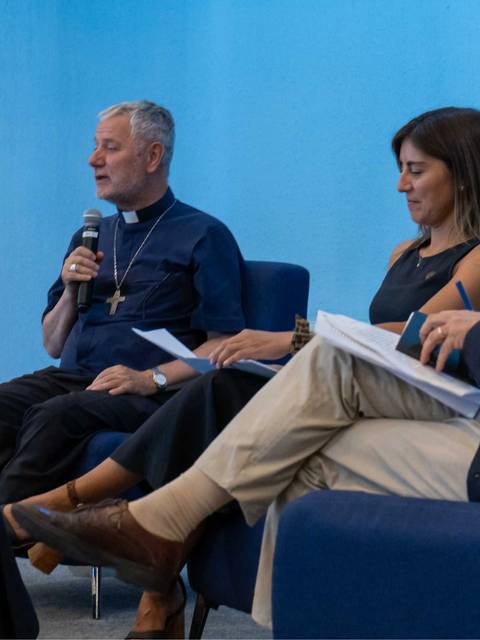 Un panel de discusión con tres personas sentadas, donde un hombre habla mientras los demás lo escuchan atentamente.