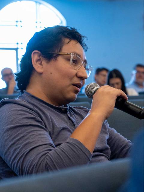 Un hombre habla por un micrófono en un ambiente de reunión.