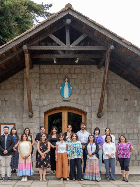 Un grupo de personas posando frente a un edificio de piedra con techo a dos aguas.