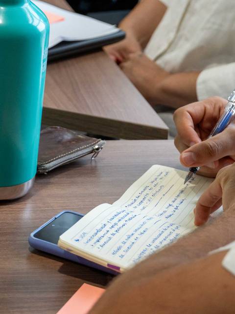 Una persona toma notas en un cuaderno mientras tiene una botella de agua y un teléfono móvil en la mesa.