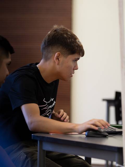 Dos jóvenes trabajan en una computadora en un entorno académico.