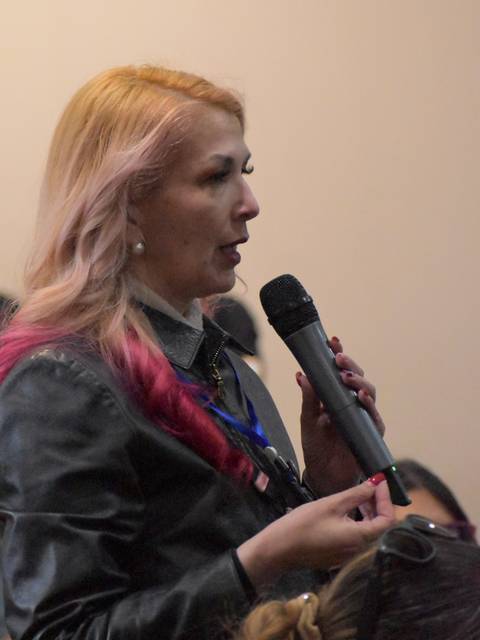 Una mujer con cabello rubio y mechas rosas habla en un micrófono durante un evento.