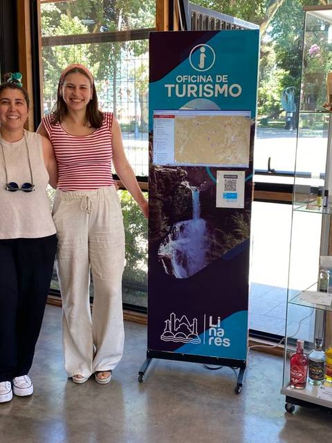 Tres personas posando junto a un banner de la oficina de turismo en un espacio interior.