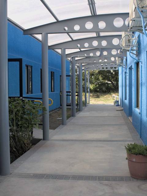 Un pasillo amplio y luminoso rodeado de muros azules y naturaleza.