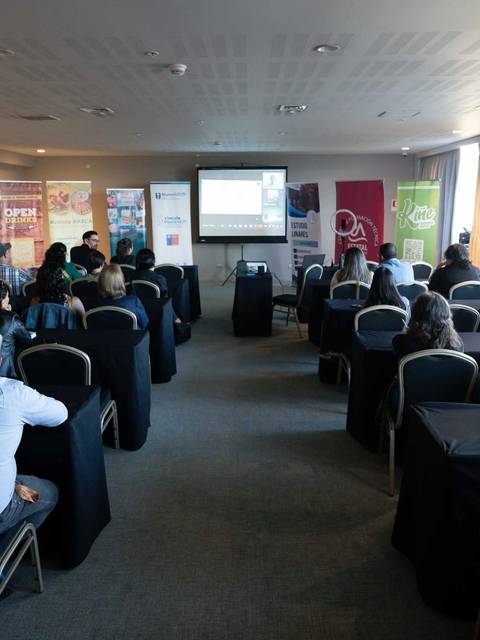 Una presentación en sala con asistentes atentos y un proyector mostrando información.