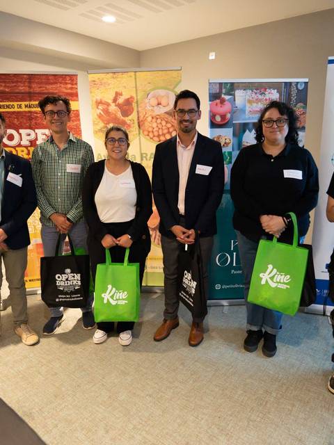 Grupo de personas sonrientes posando en un evento con bolsas verdes en la mano.