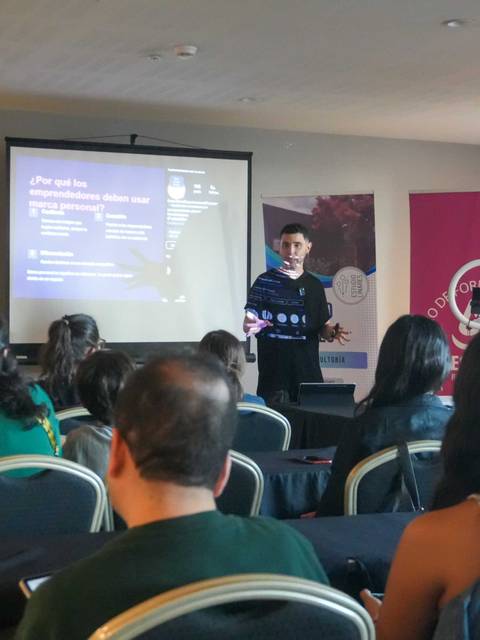 Un expositor presenta en un seminario ante un grupo de personas en una sala.