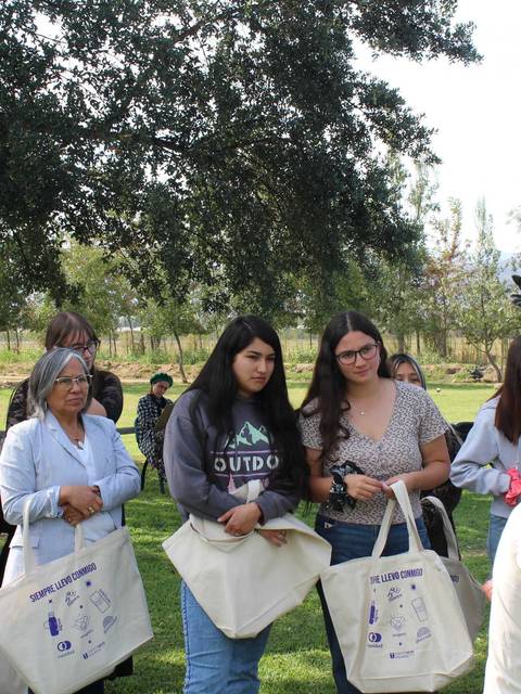 Un grupo de jóvenes escucha atentamente a una mujer que les está hablando en un día soleado en el campo.