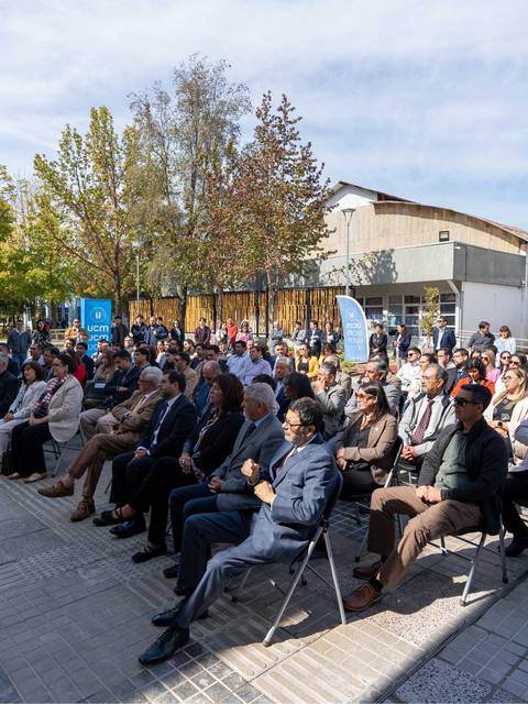Una multitud de personas sentadas en un acto al aire libre en un día soleado.