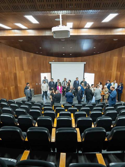 En una sala de conferencias moderna, hay un grupo de personas reunidas frente a una pantalla.