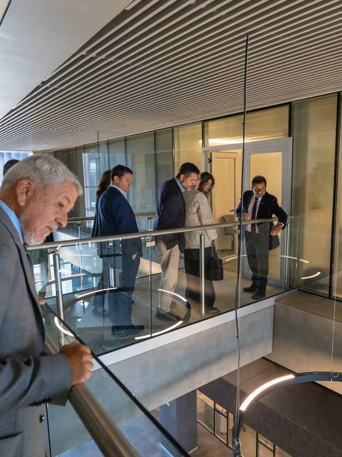 Un grupo de personas observa desde un balcón en una oficina moderna y luminosa.