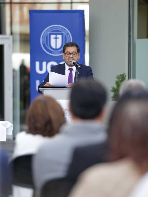 Un hombre habla en un evento al aire libre, con un formato formal, mientras la audiencia lo escucha atentamente.