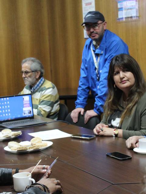 Un grupo de personas en una reunión con computadores y bocadillos en la mesa.