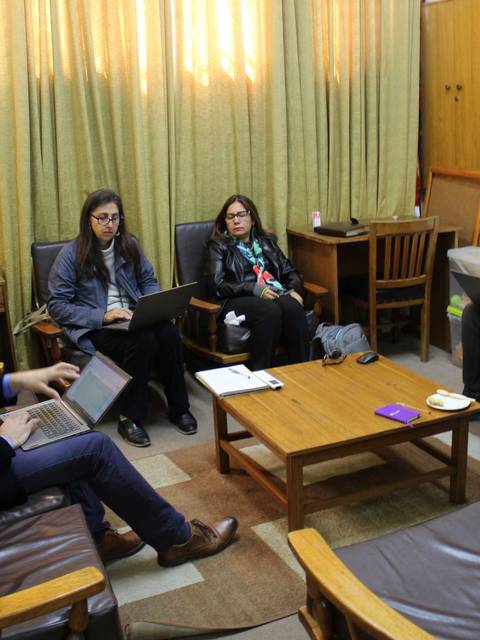 Un grupo de personas sentadas en una sala conversando y trabajando en sus computadoras.
