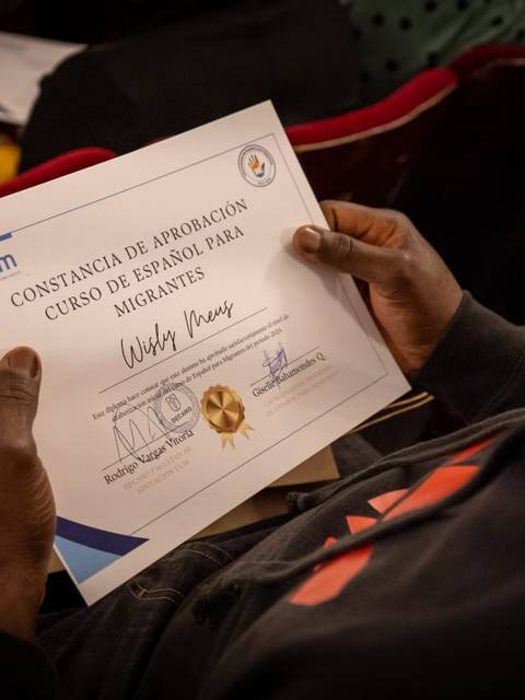 Una persona sostiene un certificado de un curso de resertificación para migrantes.