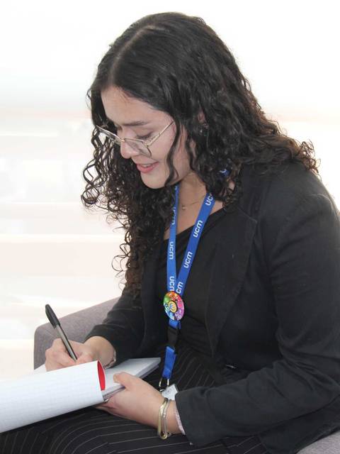 Una mujer se encuentra sentada en un sillón escribiendo en un cuaderno.