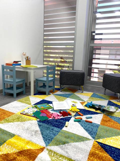 Un espacio infantil colorido con alfombra, juguetes y una mesa pequeña.