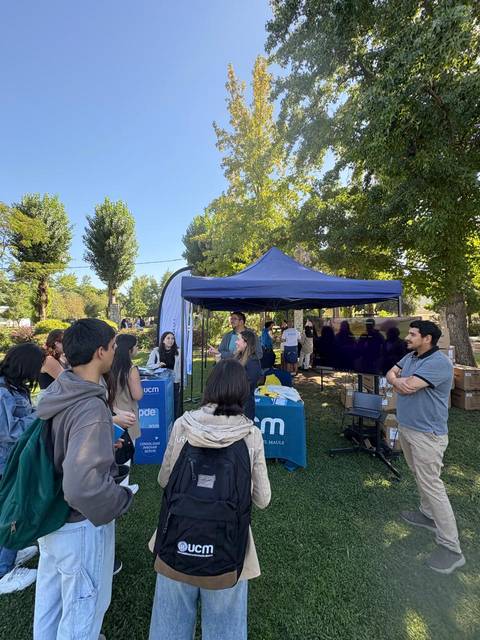 Un grupo de estudiantes escuchando a un expositor en un evento al aire libre en una universidad.