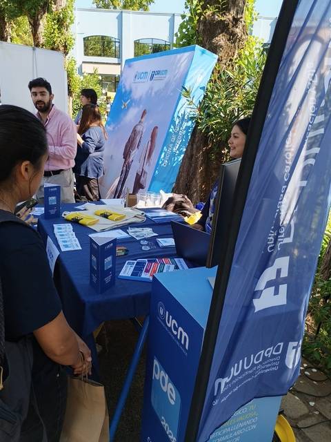 En la imagen se ve un stand de una feria con gente conversando y folletos informativos sobre educación.