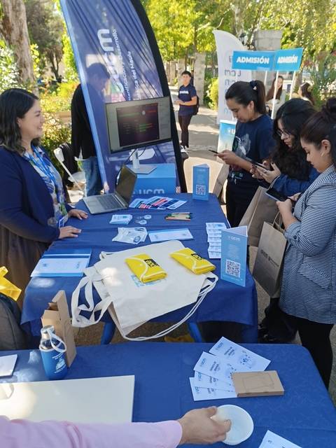 Una feria de admisión con estudiantes conversando y revisando información en un stand.