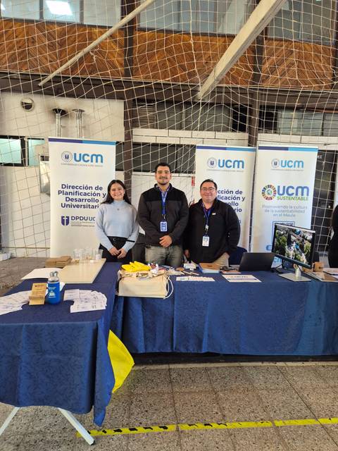 Un grupo de tres personas posando en un stand de la Universidad Católica del Maule.