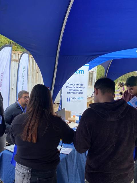 En una feria universitaria, estudiantes interactúan con representantes en un stand informativo.