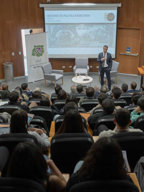 Una conferencia con un presentador frente a una audiencia atenta en un auditorio.