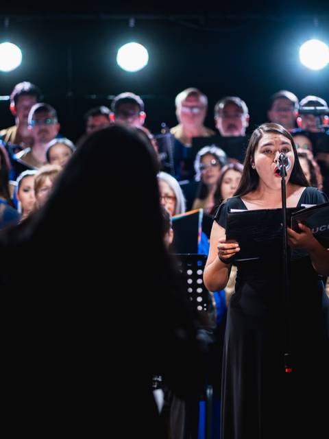 Un coro cantando con entusiasmo bajo luces brillantes.