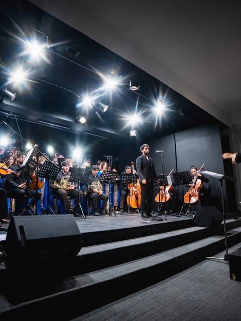 Un grupo de músicos en un concierto, bajo luces brillantes y la dirección de un director de orquesta.