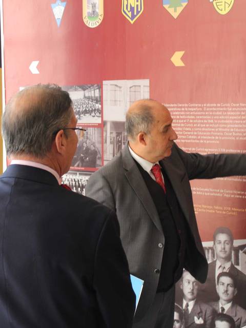 Un par de hombres conversando y señalando información en un mural educativo.